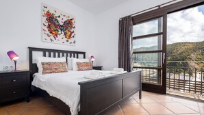 A bedroom with a bed, nightstands, a window with curtains, and a view of a hillside. - El Casar Townhouse Benahavis (Benahavis)