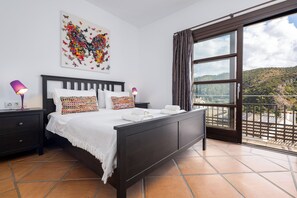 A bedroom with a bed, nightstands, a window with curtains, and a view of a hillside. - El Casar Townhouse Benahavis (Benahavis)