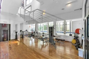 A spacious gym with various exercise equipment, large windows, and a wooden floor. - El Casar Townhouse Benahavis (Benahavis)