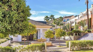A courtyard with a fountain, palm trees, and a building with a tiled roof. - El Casar Townhouse Benahavis (Benahavis)