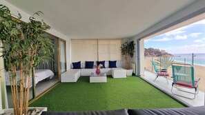 A modern living room with a green artificial turf floor, white sofas with blue cushions, a glass coffee table, and a view of the beach. - Apartment Seese Go2lloret (Lloret de Mar)