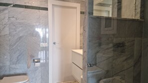A bathroom with marble walls, a white toilet, and a glass shower enclosure. - Apartment Seese Go2lloret (Lloret de Mar)