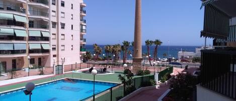 A pool area with a clear view of the ocean, a tall tower, and a multi-story building with balconies.