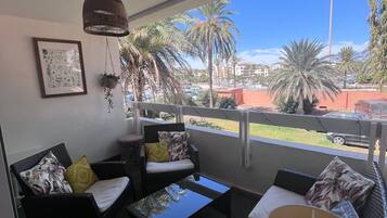 A balcony with wicker furniture, a framed picture, and a view of palm trees and buildings.