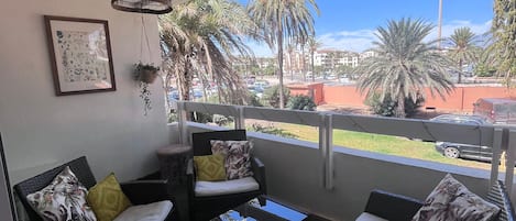 A balcony with wicker furniture, a framed picture, and a view of palm trees and buildings.