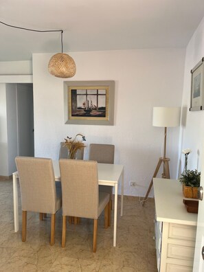 Een eethoek met een tafel, stoelen, een hanglamp, een lijst met een schilderij en een lamp.