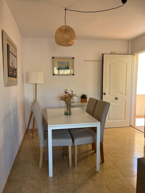 A dining area with a white table, two chairs, a hanging woven light fixture, a floor lamp, and a door. - Lovely 2 Bedroom Apartment Near the Beach (Roquetas de Mar)