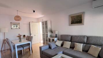 A living room with a sofa, a coffee table, a dining table with chairs, a lamp, and a picture on the wall.
