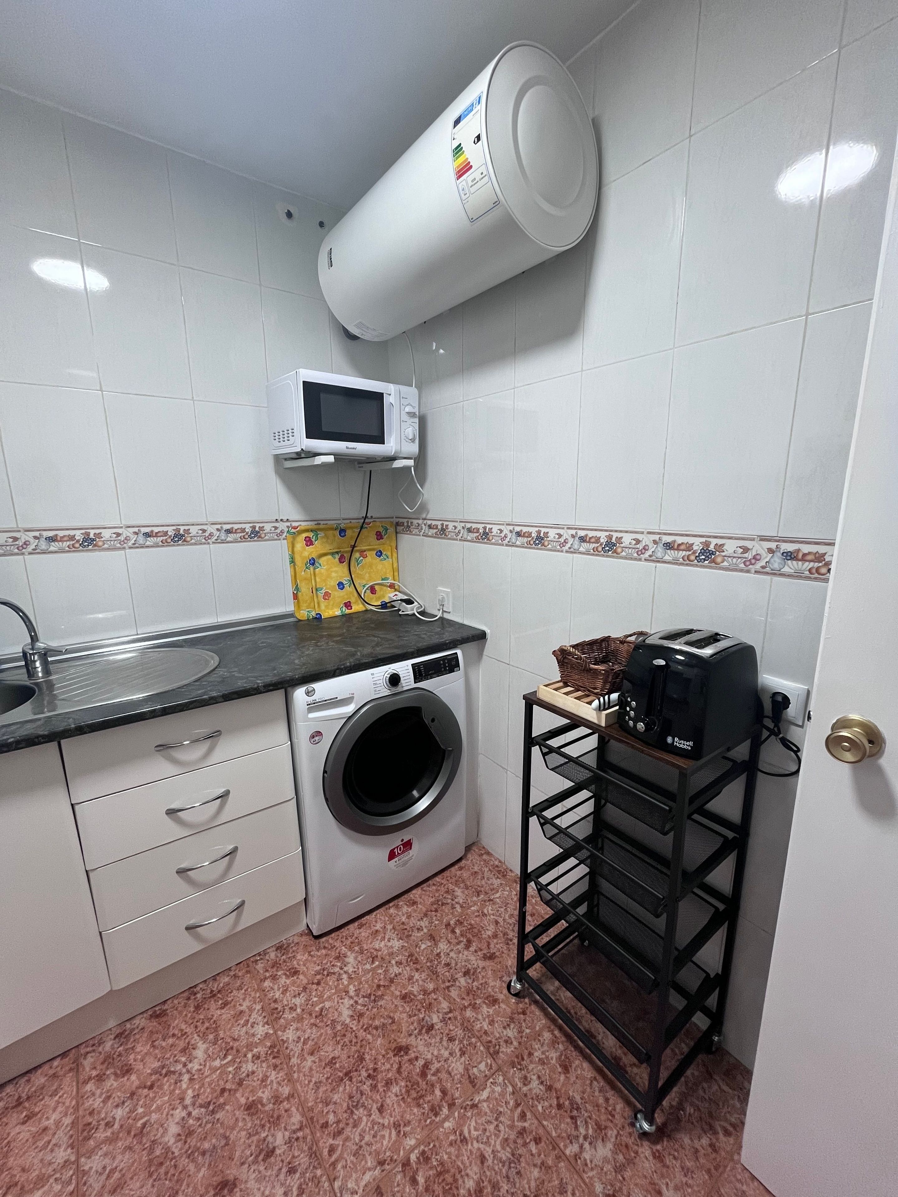 A compact kitchen with a washing machine, microwave, and toaster.