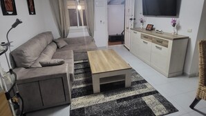 A modern living room with a sofa, coffee table, and a TV mounted on the wall. - VAO Holiday Rental-los Narejos by Oasis (Los Alcazares)