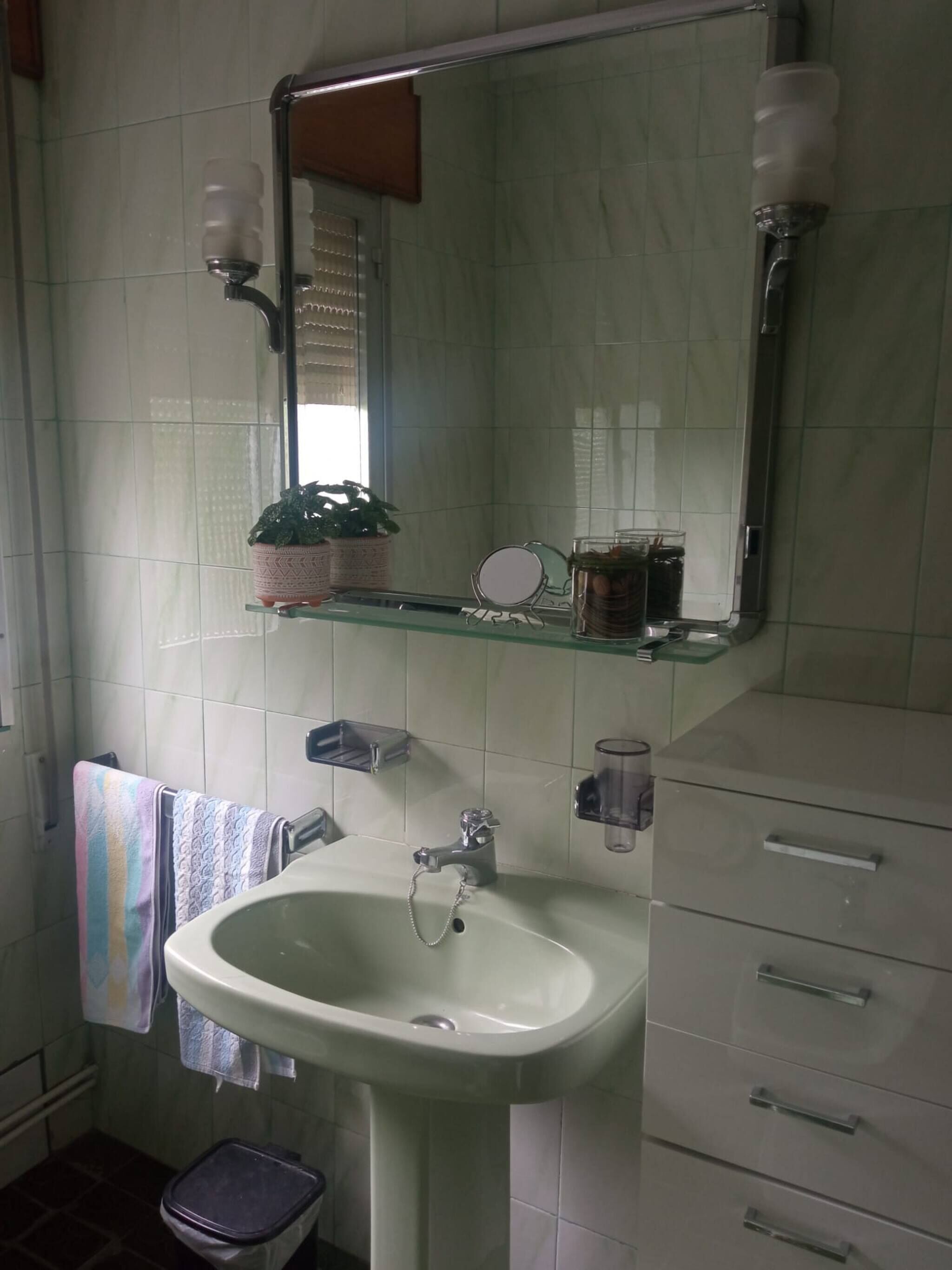 Un baño con lavamanos blanco, un espejo, toallero y un pequeño cubo de basura.
