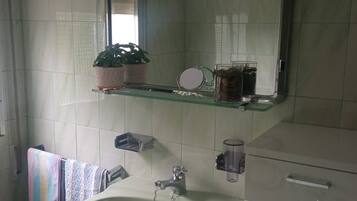 Un baño con lavamanos blanco, un espejo, toallero y un pequeño cubo de basura.