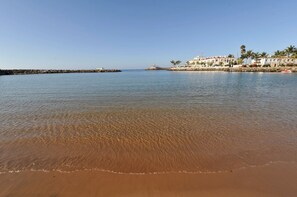 Une plage avec une eau claire, un rivage sablonneux et des bâtiments en arrière-plan.