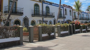 Una hilera de edificios de estilo colonial con balcones, palmeras y un cielo azul despejado.