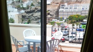 A balcony with a table and chairs, a view of a parking area, and buildings in the background. - 1 Bedroom Apartment in the Center of Puerto de Mogan (Mogan)