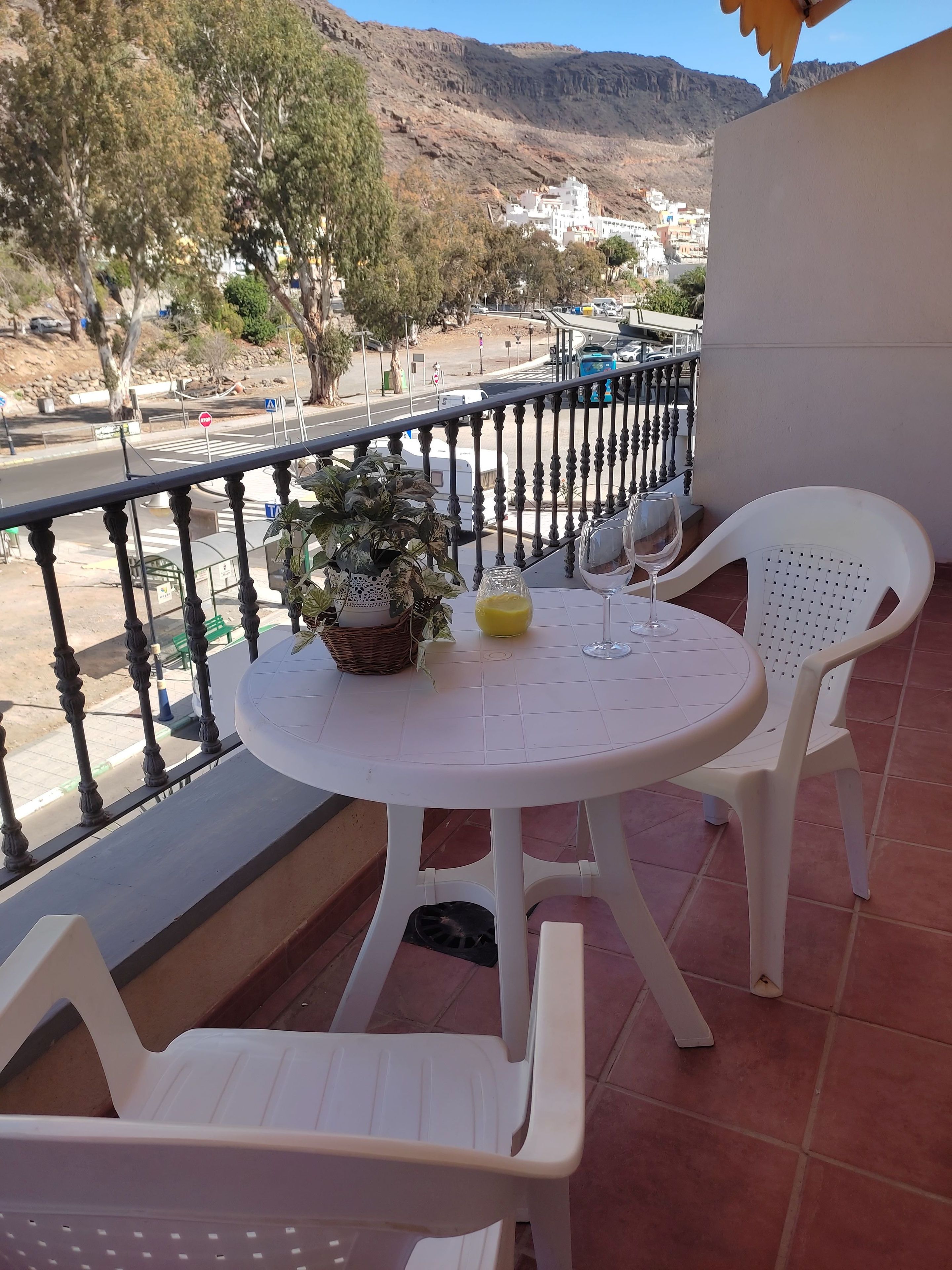 A balcony with a round table, two white plastic chairs, a potted plant, and a glass of water.