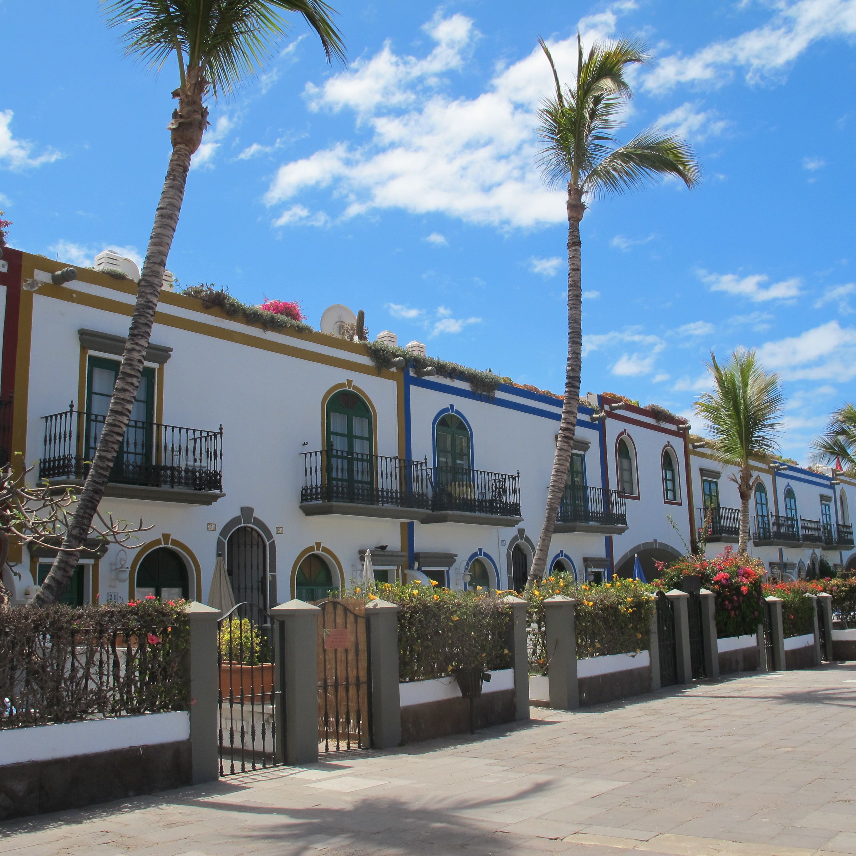 Una hilera de edificios de estilo colonial con balcones, palmeras y un cielo azul despejado.