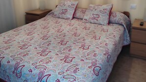 Un letto con copriletto decorato, due comodini e due quadri appesi al muro.