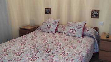 A bed with a patterned bedspread, two bedside tables, and two wall-mounted pictures.