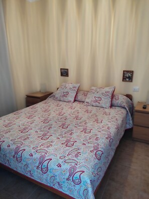 Un lit avec une couvre-lit à motifs, deux tables de chevet et deux tableaux accrochés au mur.
