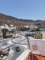Vista de un pueblo costero con edificios, una carretera y una montaña al fondo.