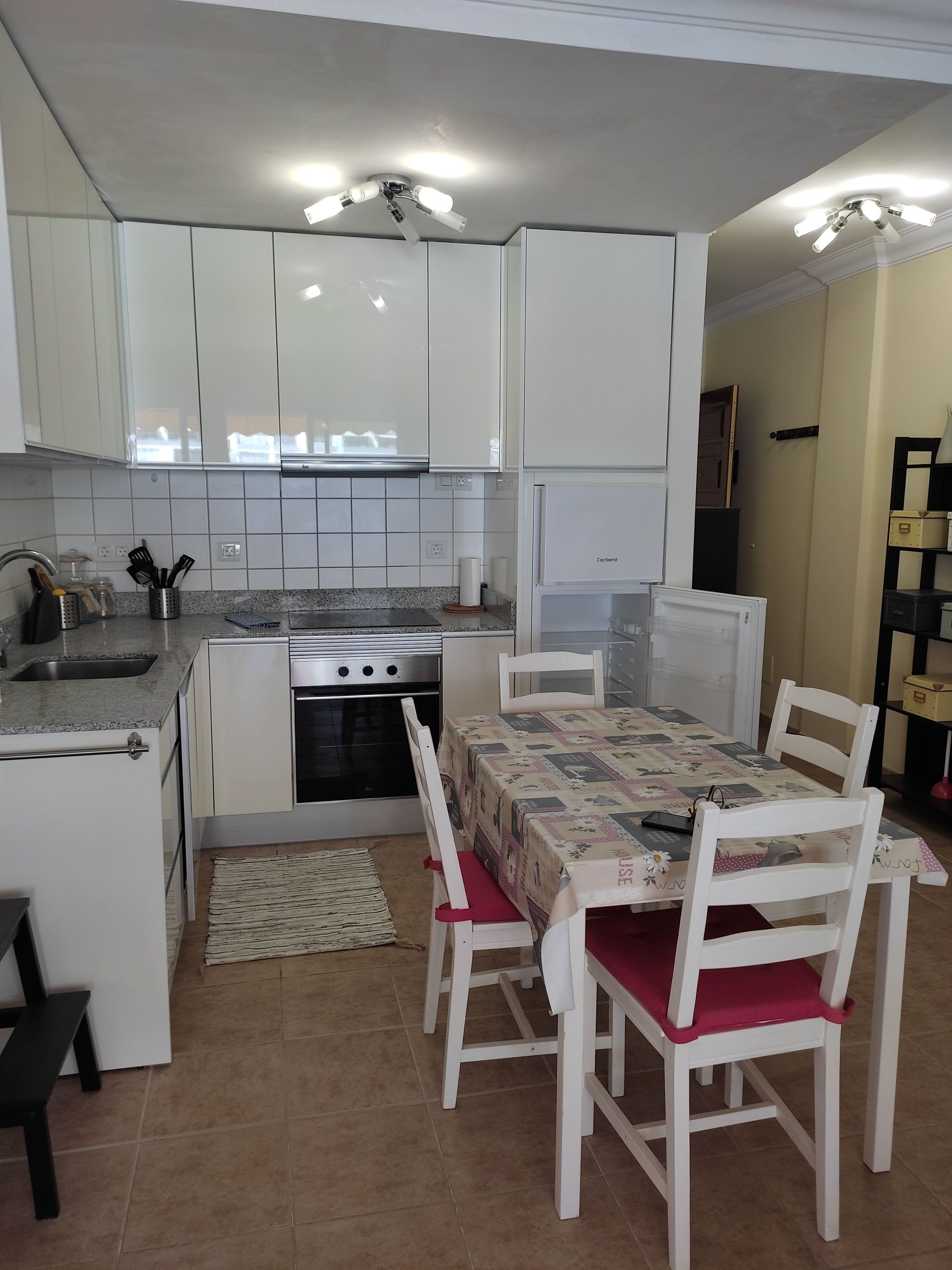 Una cocina compacta con armarios blancos, horno empotrado y una mesa de comedor con sillas.