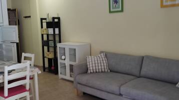 A living room with a grey sofa, a white table, and a white chair. There is a small table with a tray of items on it.