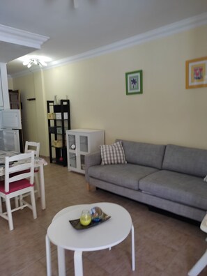 A living room with a grey sofa, a white table, and a white chair. There is a small table with a tray of items on it. - 1 Bedroom Apartment in the Center of Puerto de Mogan (Mogan)