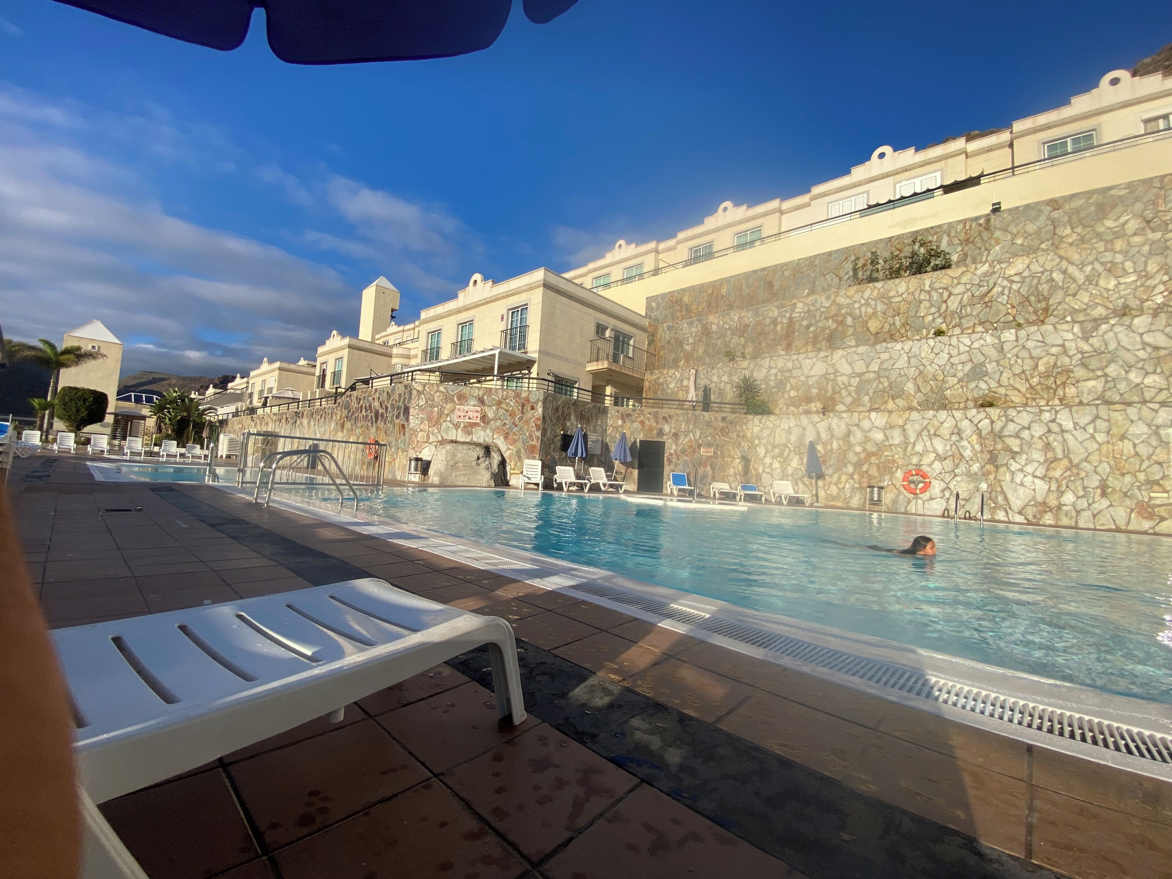 Una piscina con sillones de descanso y una pared de piedra.