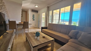 Een woonkamer met een bank, een salontafel en een televisie. Er is een eethoek met stoelen en een tafel.