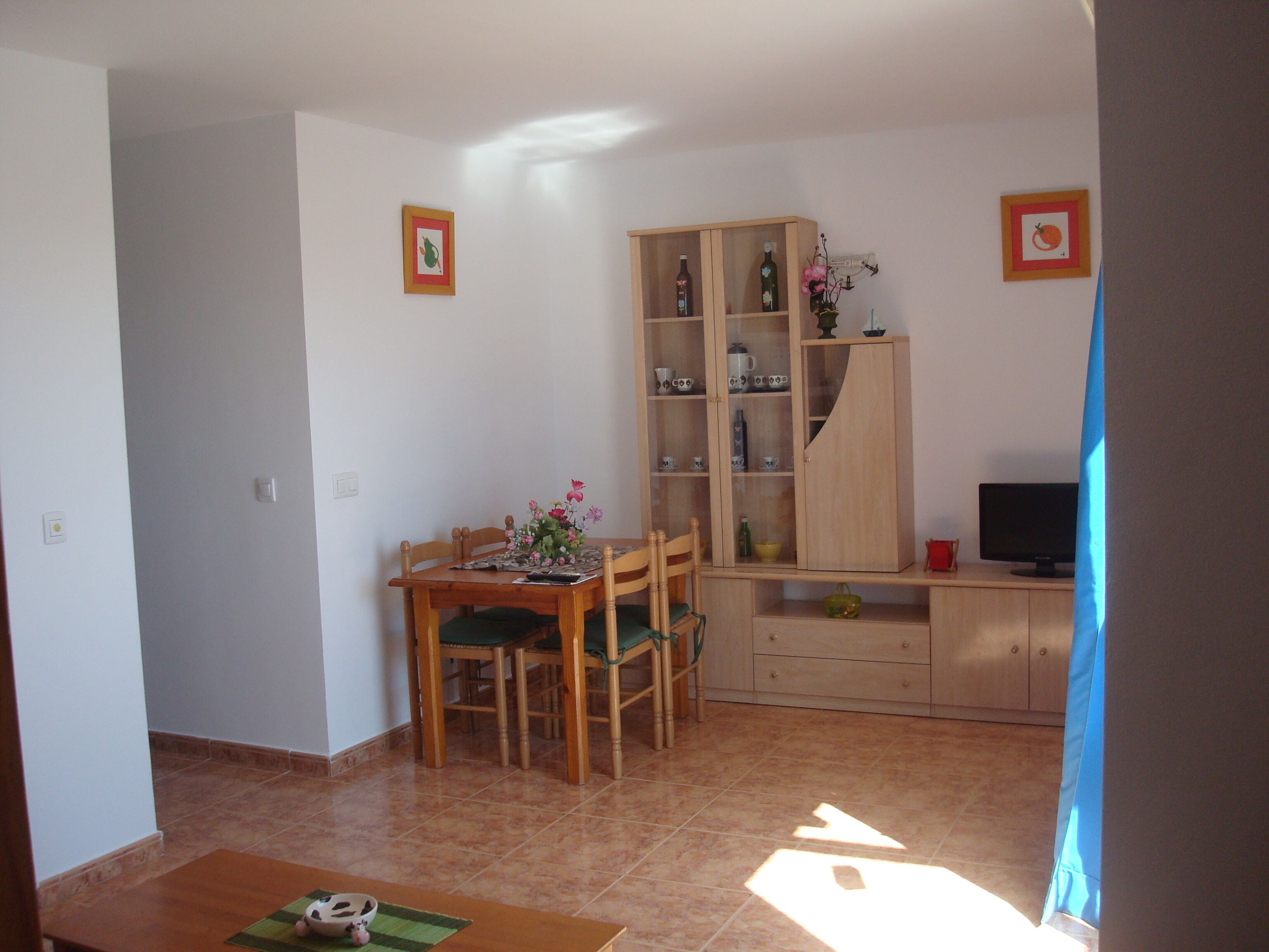 A dining area with a wooden table and chairs, a cabinet with glass doors, and a television on a stand.