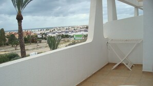 A balcony with a view of a coastal town, a white folding table, and a palm tree. - Impressive Apartment in Ground Floor With Terrace of 2 Rooms, A A and Pool 4 (Vera)
