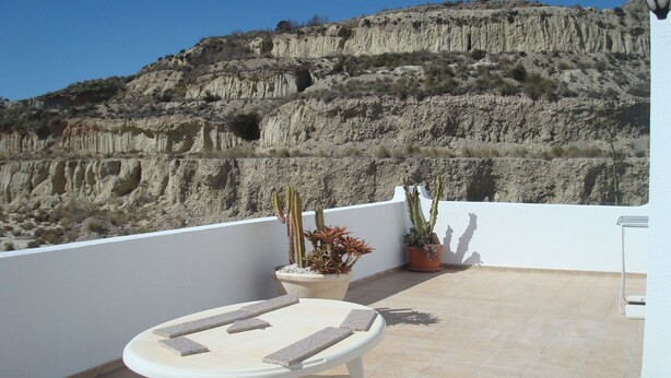 A terrace with a table and chairs, potted plants, and a view of a rocky hillside. - Impressive Apartment With Terrace and two Rooms, AC and Pool (Vera)