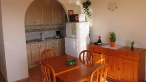 A compact kitchen with wooden cabinets, a dining table with chairs, and a refrigerator. - Impressive Apartment With Terrace and two Rooms, AC and Pool (Vera)