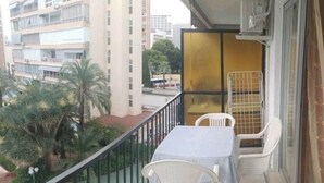 Ein Balkon mit Tisch und Stühlen, Blick auf Palmen und ein Gebäude im Hintergrund.