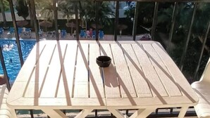 Ein Balkon mit weißem Tisch und Stühlen, mit Blick auf einen Swimmingpool und die Stadtlandschaft.
