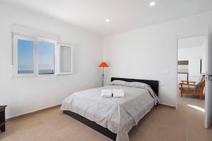 A bedroom with a bed, a nightstand, a lamp, and a view of the sea through a window. - Finca Casa Eva Entire Accommodation (Granadilla de Abona)