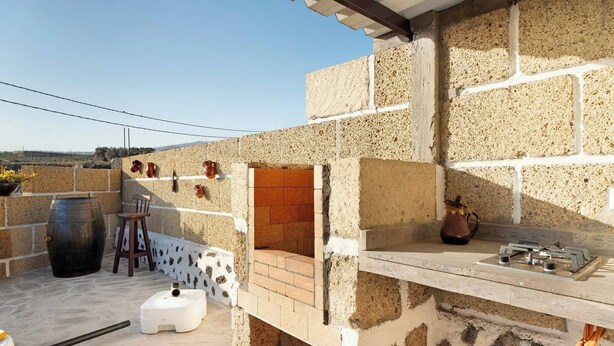 Un patio con muro de piedra, horno de ladrillo, estufa a gas y un barril negro grande.