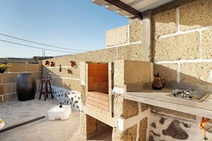 Eine Terrasse mit Steinmauer, Lehmofen, Gasherd und einem großen schwarzen Fass.