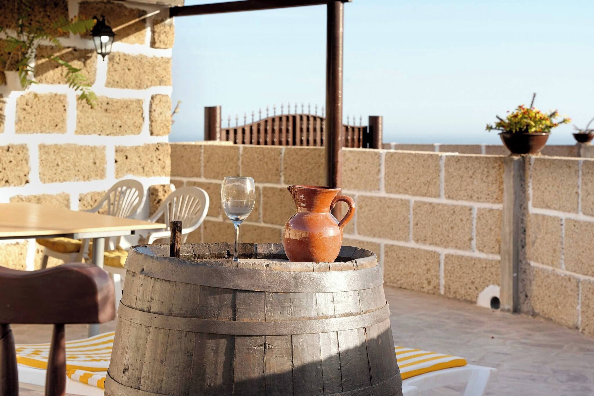 A rustic outdoor seating area with a wooden barrel, a clay jug, and a glass of water.