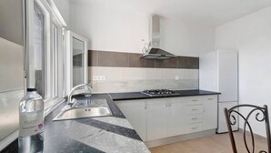 Una cocina con estufa a gas, pileta de acero inoxidable y alacenas blancas.