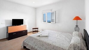Un dormitorio con una cama, un televisor sobre un mueble, una ventana y una lámpara de pie.