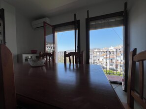 A dining area with a wooden table and chairs, a glass bowl, and a view of buildings through large windows. - Cd-2063 Three Bedroom With Roof Terrace (Frigiliana)