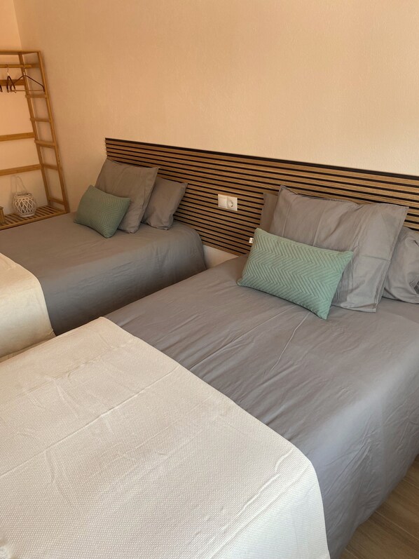 Une chambre d’hôtel avec deux lits, chacun doté de draps gris et de plusieurs oreillers. On y trouve une tête de lit en bois, une petite table sur laquelle est posée une lanterne blanche, et une échelle en bois appuyée contre le mur.