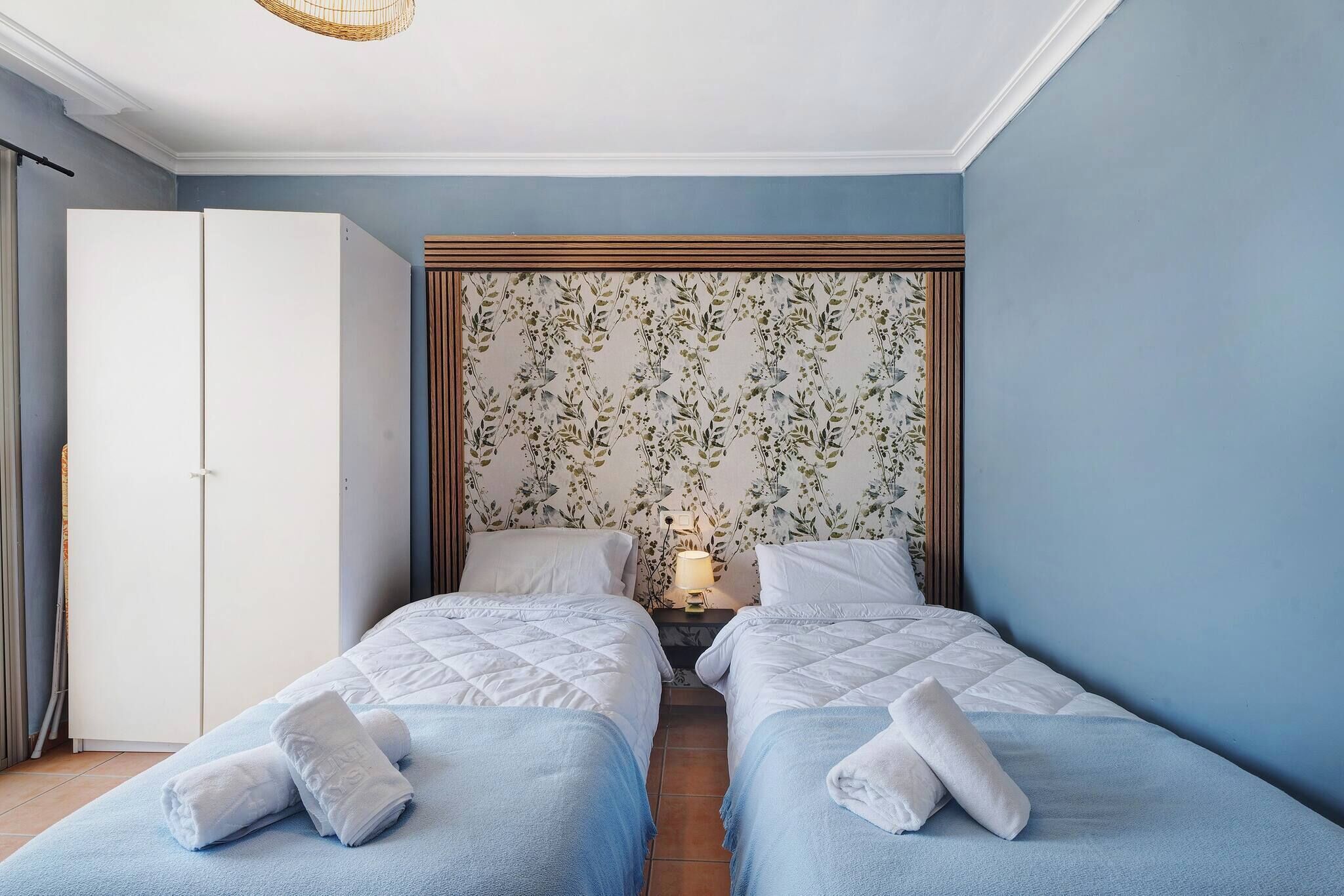 A room with two beds, a wardrobe, and a floral-patterned headboard.