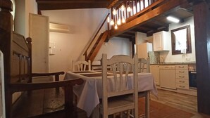 Ein Essbereich mit Holztisch und Stühlen, eine Treppe mit sichtbaren Balken und eine Küche mit weißen Schränken und einem Fenster.