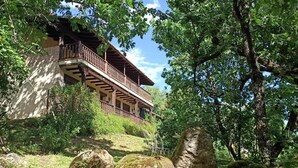 Ein rustikales Holzgebäude mit Balkon, umgeben von üppigem Grün und großen Felsen.