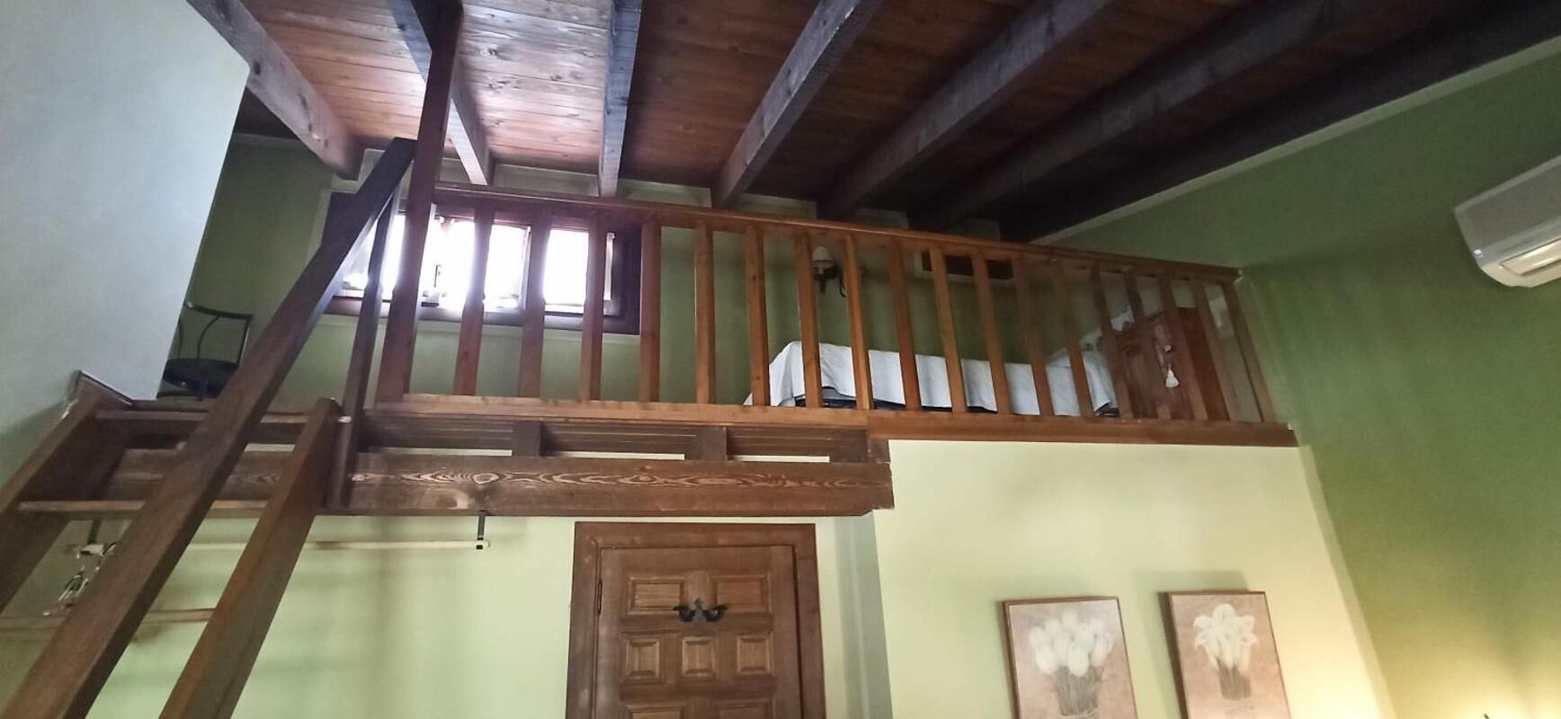 A wooden staircase with a railing leading to a lofted area. A wooden door is visible below the staircase.