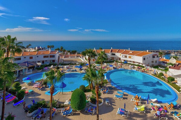 Relax by the resort's central pool surrounded by lounge areas and palm trees.