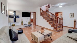 A spacious living room with a wooden staircase, a flat-screen TV mounted on the wall, and a coffee table with decorative items. - Beautiful Arianny House With Pool (Arona)